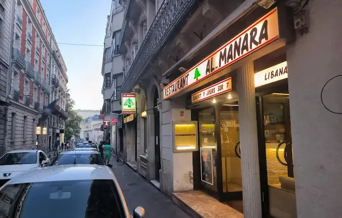 Façade sobre et chaleureuse du restaurant libanais Al Manara à Montpellier, avec vitrine éclairée et murs blancs.