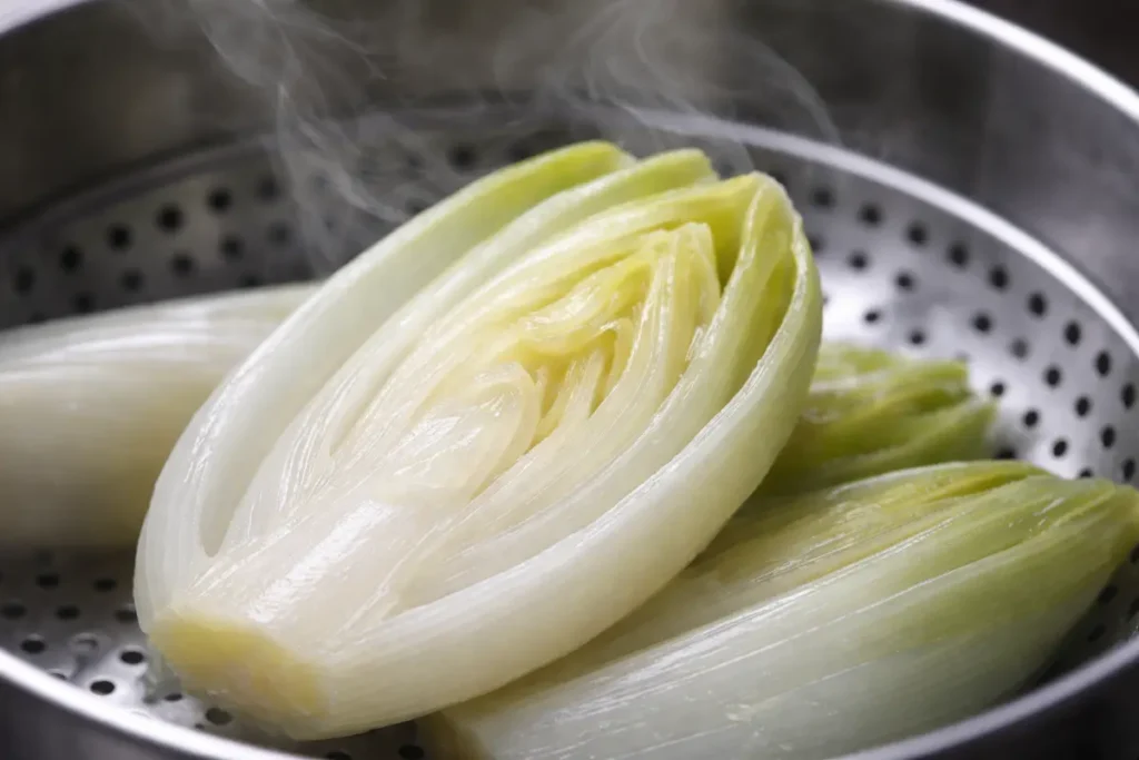 Gros plan sur des endives disposées dans un panier vapeur en inox, montrant une couleur blanc nacré et des gouttelettes d'eau.